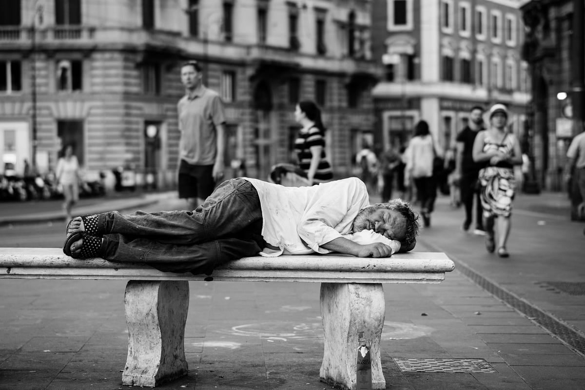 A homeless man sleeping on a bank in the city.