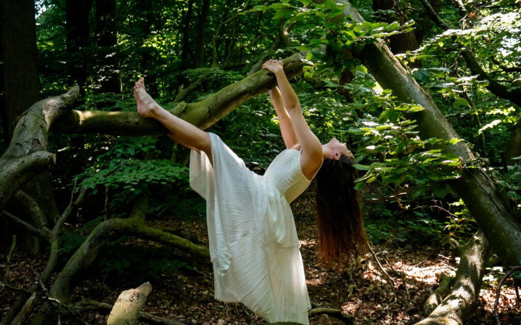 a-woman-in-a-white-dress-standing-on-a-branch-in-the-woods