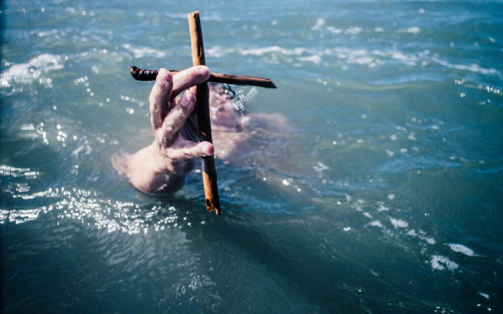 Person under water holding a wooden cross.